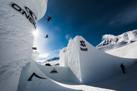 Snowboarderin und Schifahrerin springen über eine Schneeburg